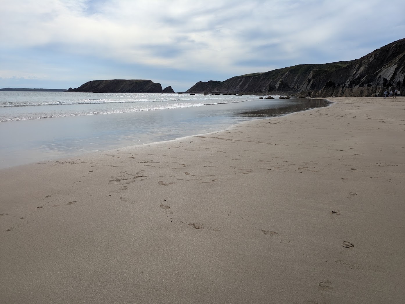 A wide sandy beach with cliffs and breaking surf